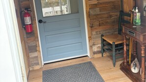 Ein Holzblockhaus-Interieur mit einer blauen Tür, einem Feuerlöscher, einem Stuhl und einem kleinen Tisch mit einer Flasche.