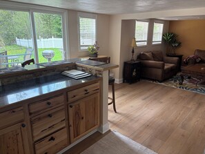 A kitchen with a granite countertop, wooden cabinets, and a view of the backyard. - Boardman River Cottage, 2 bedroom 1 Bath steps away from the banks of the river (Traverse City)