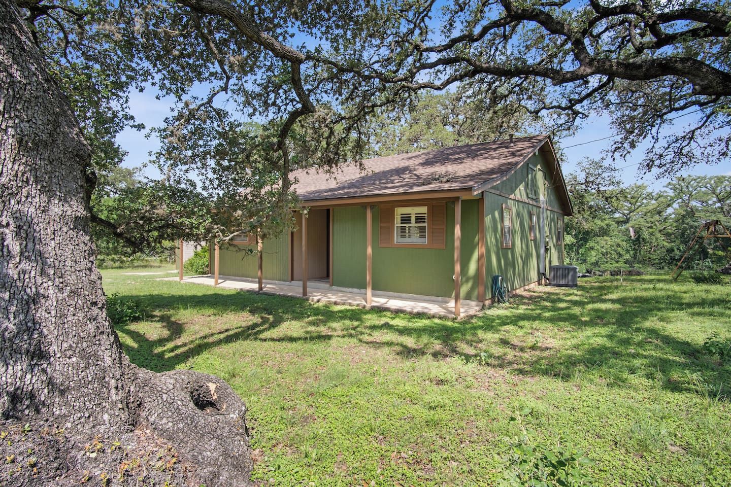 A single-story building with a green exterior and a brown roof, surrounded by grass and trees.