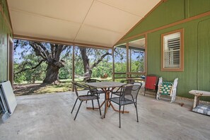 Eine Terrasse im Freien mit Tisch und Stühlen, einem überdachten Bereich und Blick auf Bäume und Grün.