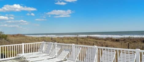 A deck with white lounge chairs overlooking a beach and ocean.