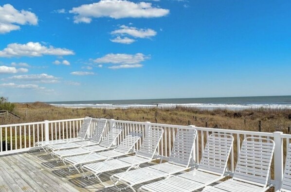 A deck with white lounge chairs overlooking a beach and ocean.