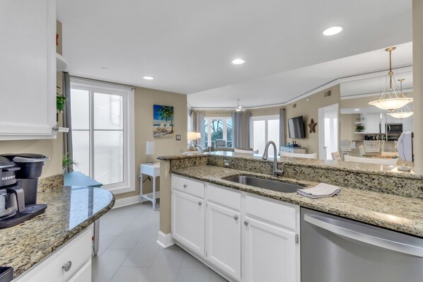 A modern kitchen with granite countertops, white cabinetry, and a stainless steel sink.