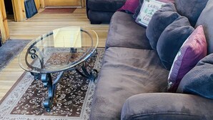 A cozy living room with wooden walls, a dark gray sofa, a glass coffee table, and a patterned rug.