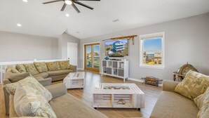A spacious living room with a sectional sofa, a coffee table, and a television mounted on the wall. - Oceanview Dog Friendly w/ Private Pool, Hot Tub, Wet Bar. Shore Beats Workin' (Frisco)