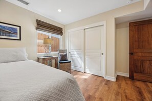 Une chambre à coucher avec un lit, une table de chevet, une lampe, une chaise en osier et une porte.