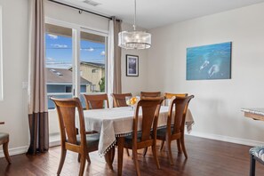 Un coin repas avec une table dressée pour six personnes, des chaises en bois, un lustre et un tableau représentant des dauphins au mur.