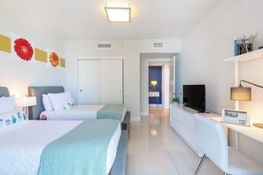 Habitación de hotel moderna con dos camas, un escritorio, un televisor y un baño visible al fondo.