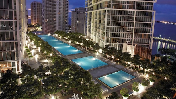 Un edificio de gran altura con piscina en la azotea, rodeado de árboles y sillones de descanso.