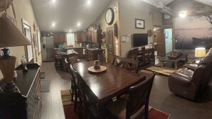 A spacious living area with a dining table, leather sofa, and a TV. - Cozy Cabin in the Woods - Lake Livingston, Texas (Livingston)