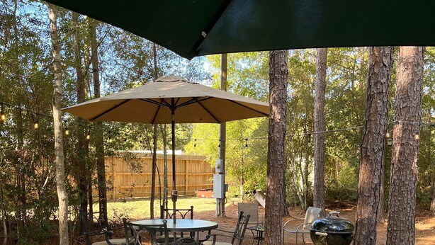 A hot tub under a covered patio with a table and chairs, surrounded by trees. - Cozy Cabin in the Woods - Lake Livingston, Texas (Livingston)