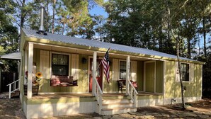 A single-story house with a porch, a chimney, and an American flag. - Cozy Cabin in the Woods - Lake Livingston, Texas (Livingston)