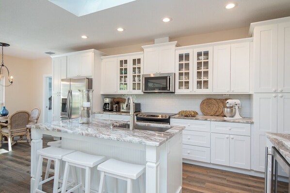 Una cocina moderna con muebles blancos, una isla grande con taburetes de bar, electrodomésticos de acero inoxidable y una barra desayunadora.