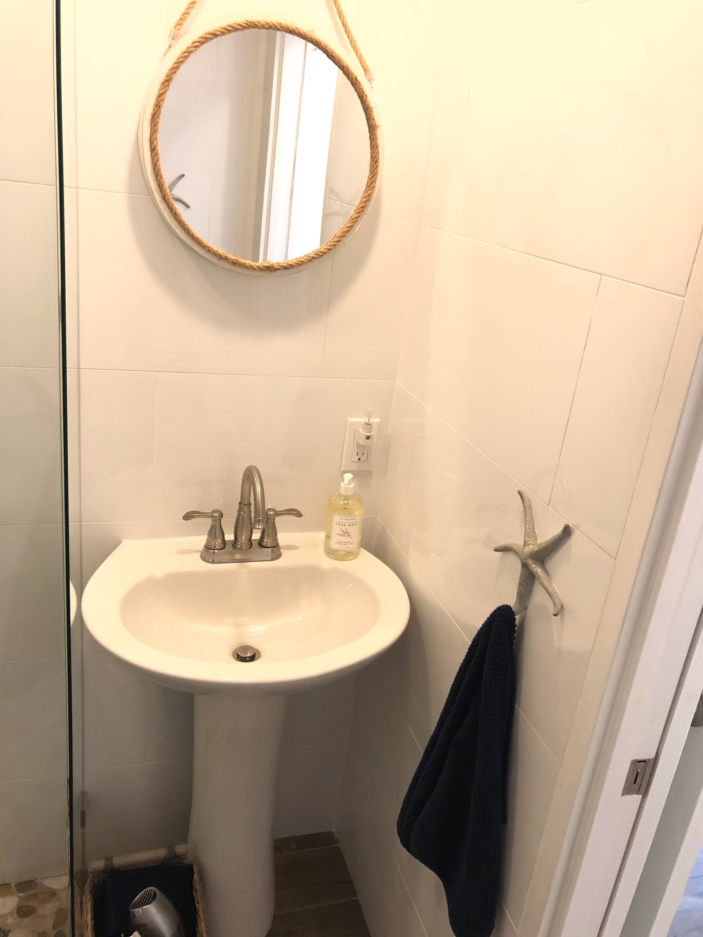Un baño con un espejo redondo, un lavabo, dispensador de jabón y un perchero para toallas.