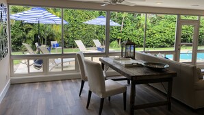 Een ruim terras met een eettafel, stoelen en uitzicht op een zwembad en weelderige begroeiing.