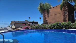 Una piscina con superficie d'acqua cristallina e azzurra, circondata da un bordo bianco e una piccola parte di un edificio con un muro marrone e una finestra.