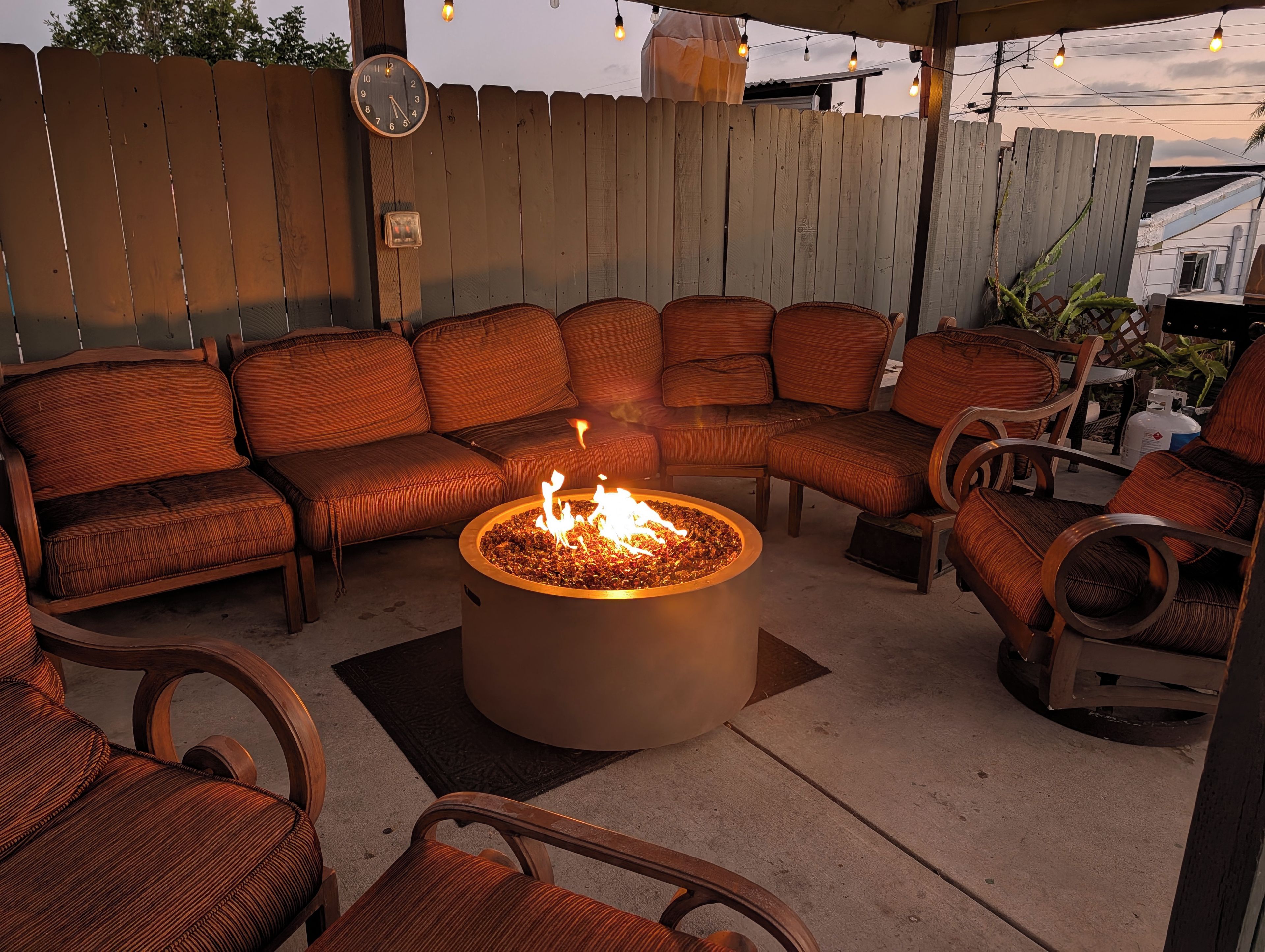 An outdoor seating area with a fire pit, cushioned chairs, and a wooden fence.