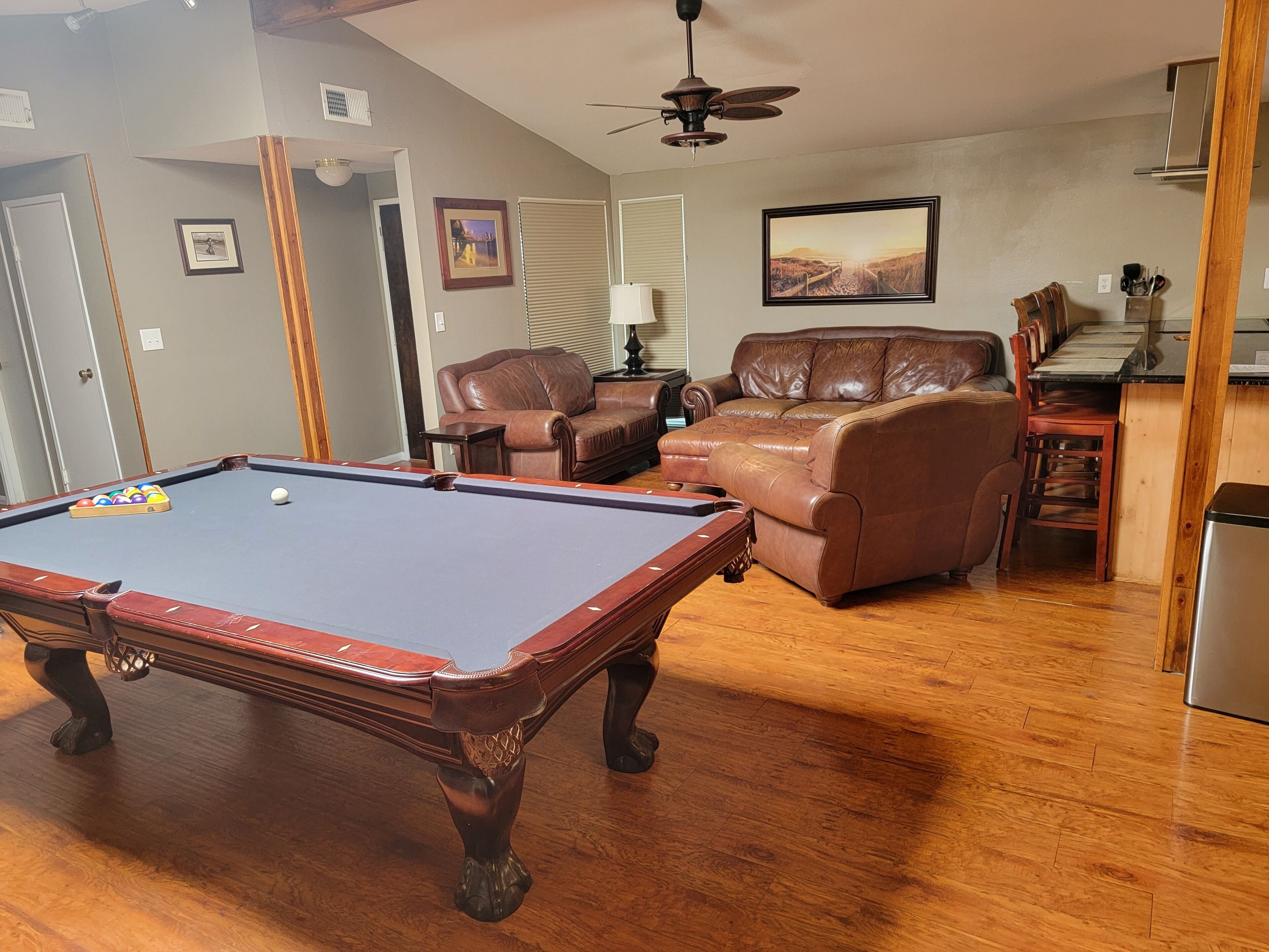 A living room with a pool table, leather sofas, a dining area, and a kitchen.