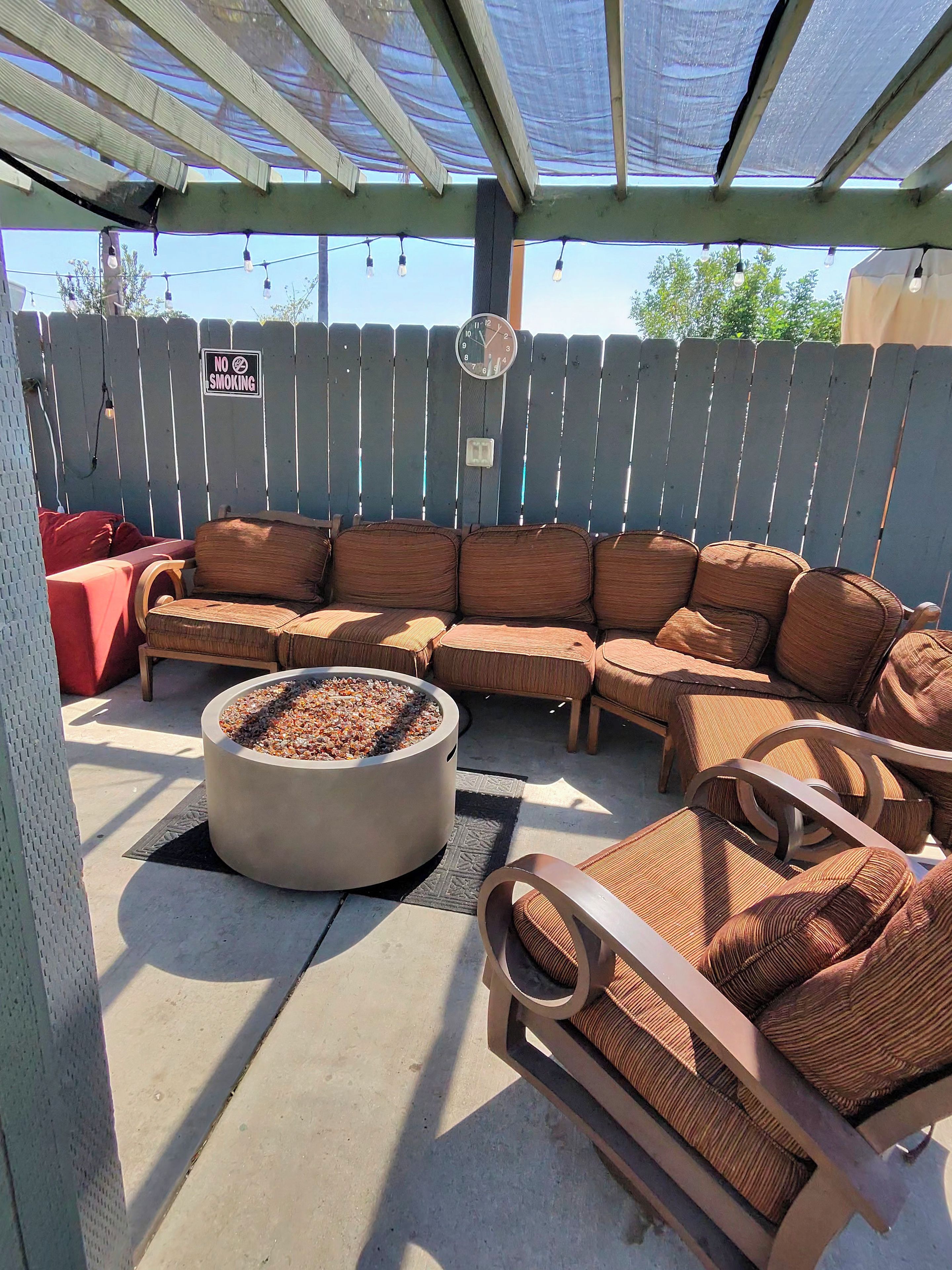 A covered outdoor seating area with a fire pit, wooden furniture, and a 'No Smoking' sign on a fence.