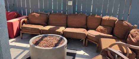 A covered outdoor seating area with a fire pit, wooden furniture, and a 'No Smoking' sign on a fence.