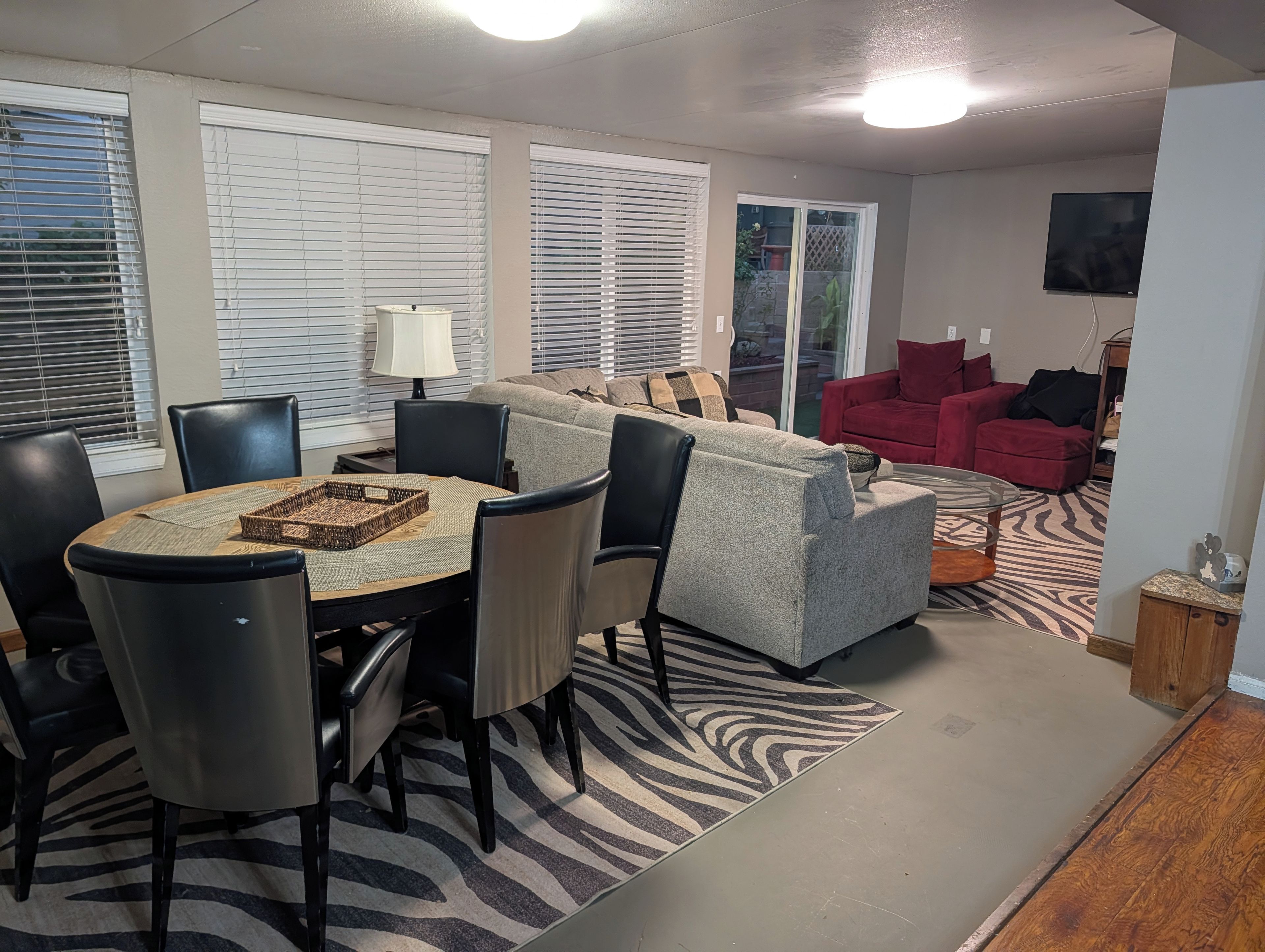 A living room with a grey sofa, red armchairs, a zebra-patterned rug, and a dining area with a round table and chairs.