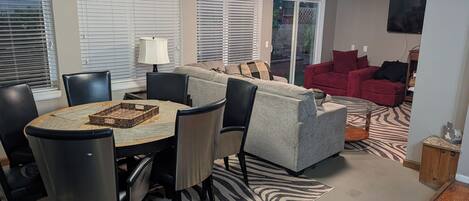 A living room with a grey sofa, red armchairs, a zebra-patterned rug, and a dining area with a round table and chairs.