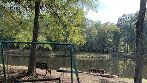 Um parque com baloiço, bancos e um lago tranquilo rodeado de árvores.