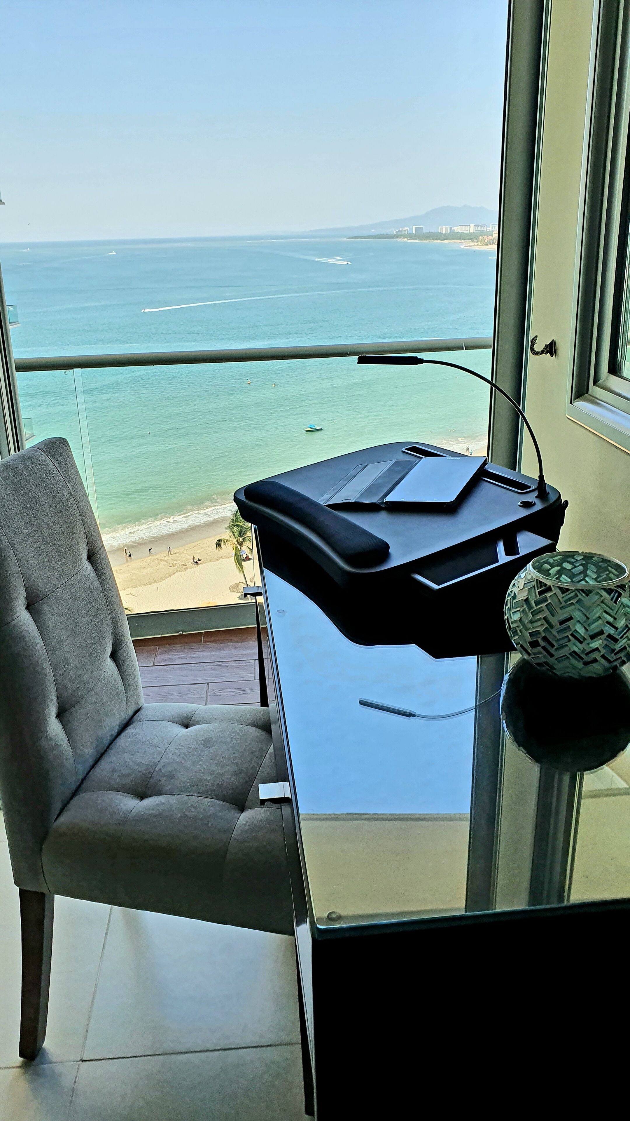 A balcony with a view of the ocean, a chair, and a small table with a decorative bowl.