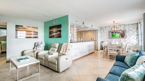 A spacious living area with a sofa, a massage chair, a dining table, and a kitchen area with a white countertop. - Dockside 504 with private balcony and beautiful views (Clearwater)