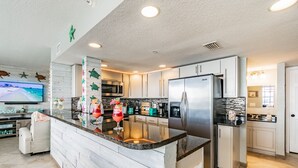 A modern kitchen with white cabinetry, a central island, stainless steel appliances, and a flat-screen TV mounted on the wall. - Dockside 504 with private balcony and beautiful views (Clearwater)