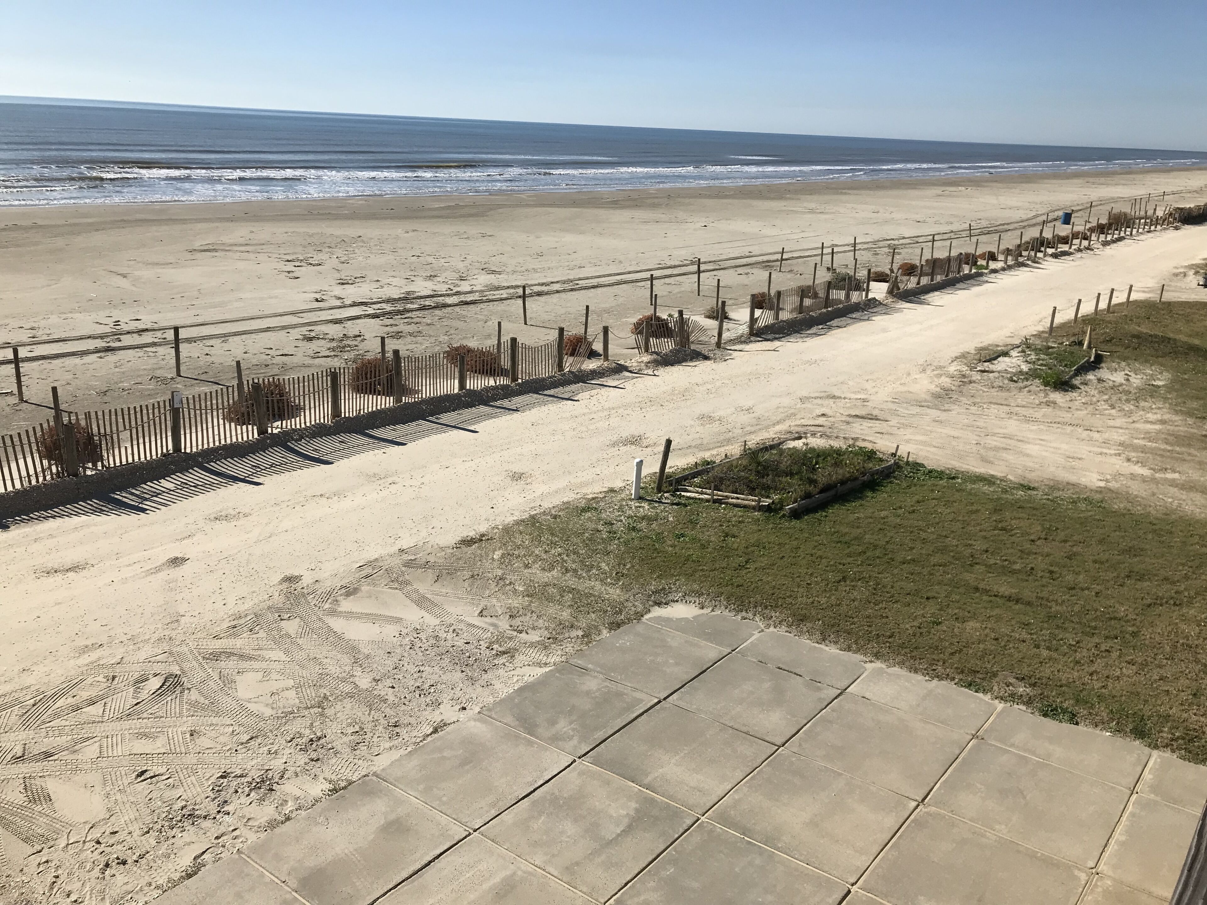 A beach with a paved walkway, a wooden fence, and a grassy area.