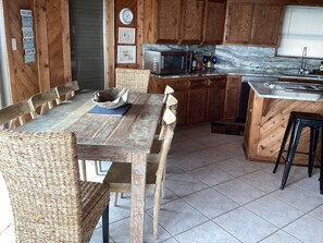A rustic kitchen with wooden cabinets, a dining table with wicker chairs, a woven bowl, and a clock on the wall. - Beach front,  3/2 in the house with a 3rd bath downstairs in the garage (Galveston)