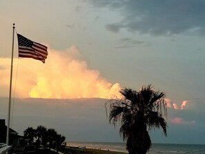 An American flag on a flagpole, a palm tree, and a view of the ocean with a sunset. - Beach front,  3/2 in the house with a 3rd bath downstairs in the garage (Galveston)
