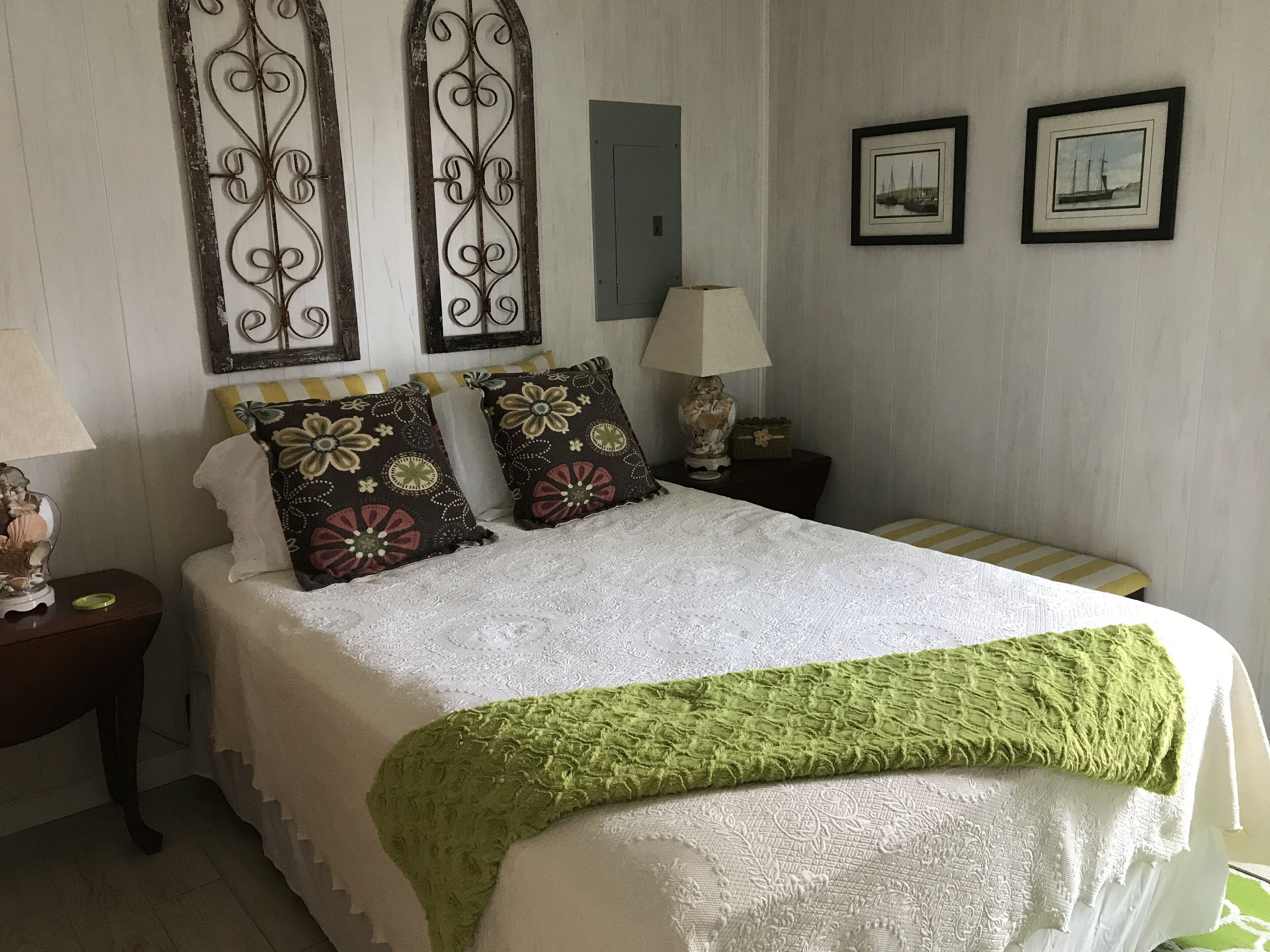 A neatly made bed with floral pillows, a green throw blanket, and a nightstand with a lamp and decorative items.