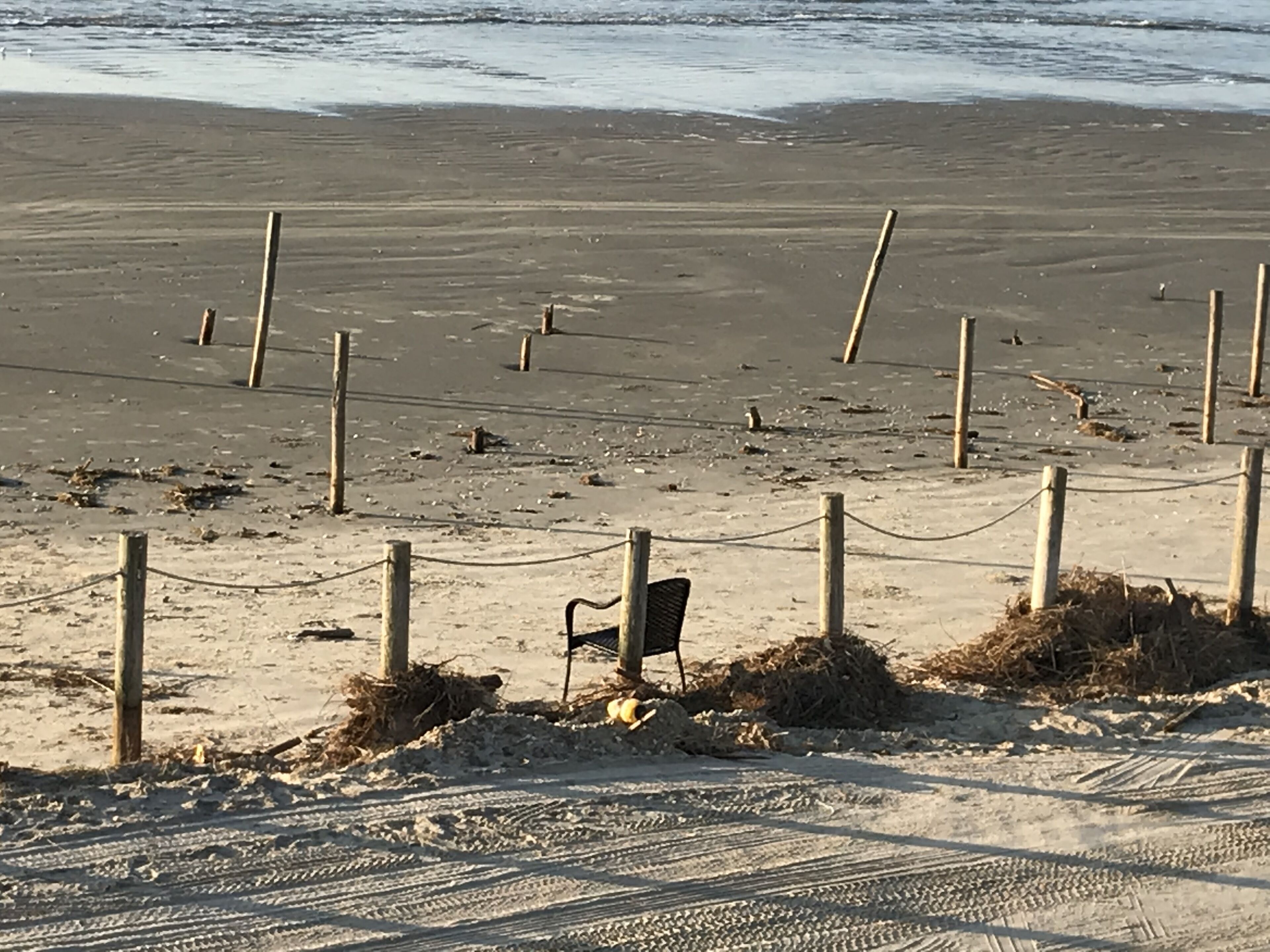 A sandy beach with wooden posts and a chain-link fence.