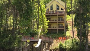 Un immeuble jaune à plusieurs étages, doté d’un balcon à l’étage supérieur, et entouré d’une forêt dense.