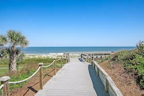A wooden boardwalk leading to a beach with a clear sky.