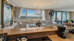 Una cocina con vista al océano, una araña y un comedor con mesa y sillas.