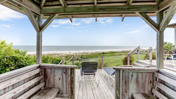 Una terraza de madera con vista a la playa, bancos de madera y una barandilla de cuerda.