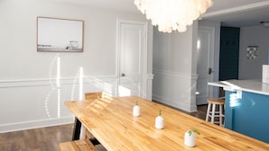 A modern kitchen with a wooden dining table, white cabinets, and a blue accent wall. - Beach Cottage Multiple Suites & Walk to Boardwalk! (Virginia Beach)