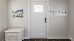 A white door with a small window, a wall-mounted coat rack, a framed picture, and a white cabinet with doors. - Beach Cottage Multiple Suites & Walk to Boardwalk! (Virginia Beach)