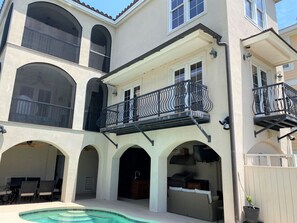 A multi-story house with a pool, outdoor seating, and a balcony with a wrought iron railing.