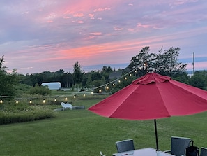 An outdoor patio with a red umbrella, string lights, and a table with chairs. - Stunning home near Sandbanks -  Picton - Prince Edward County (Prince Edward)