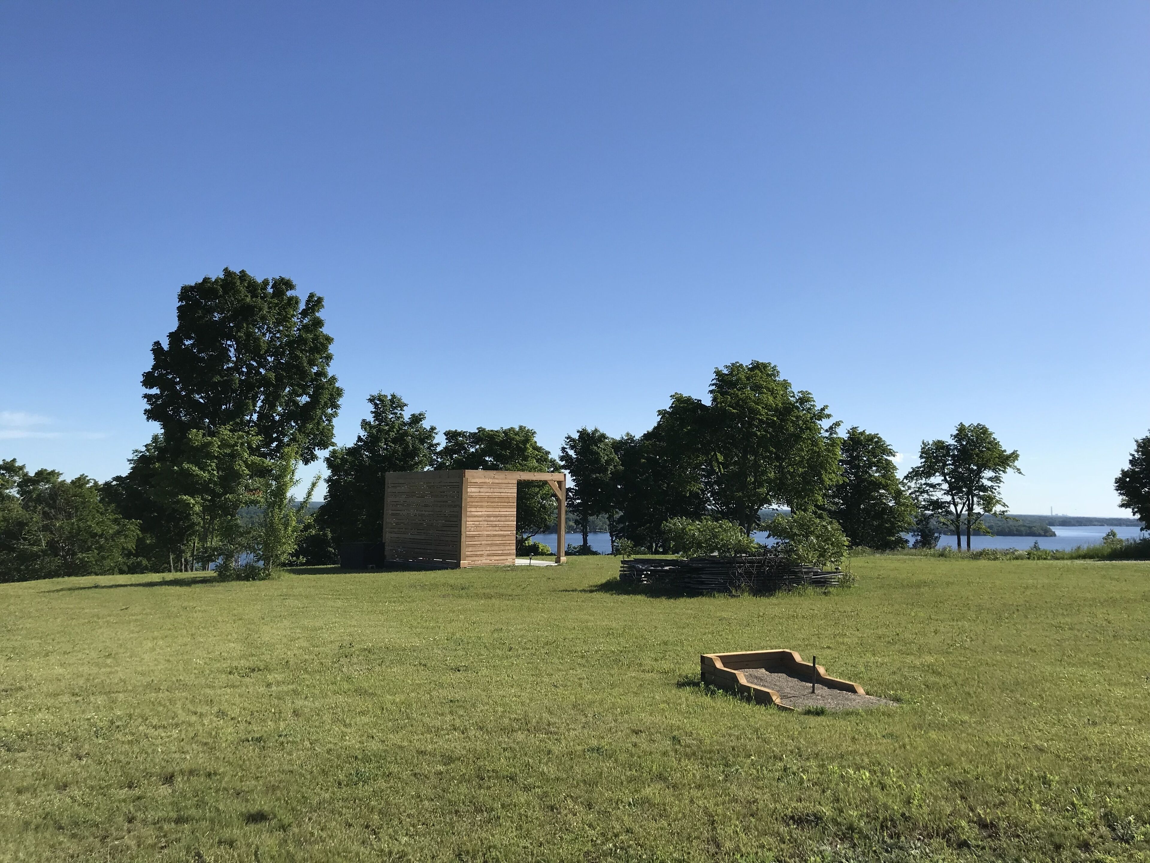 A grassy field with a small wooden structure and a tree in the background.
