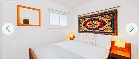 A bedroom with a bed, a mirror, a window, and a wall tapestry.