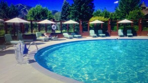 A swimming pool with lounge chairs and umbrellas, surrounded by trees.