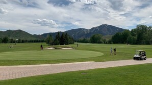 A golf course with a paved path, green grass, and distant mountains.
