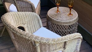 A wicker chair and table set on a wooden deck with a glass of wine on the table.
