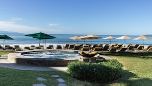 Zona de piscina con sillones de descanso y sombrillas, un jacuzzi y vistas al océano.