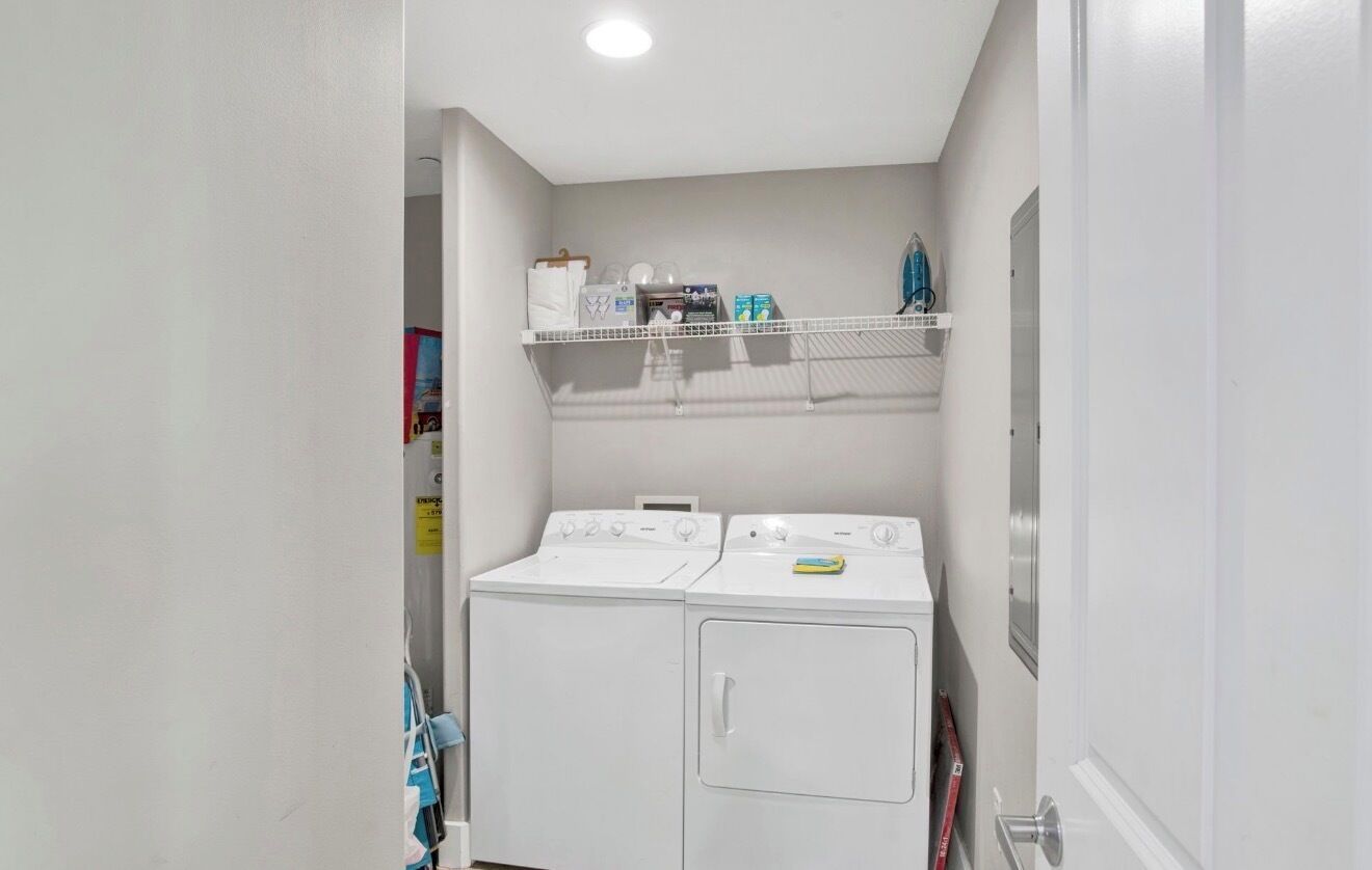 Une buanderie avec deux machines à laver blanches et une étagère au-dessus, sur laquelle sont rangés divers objets.